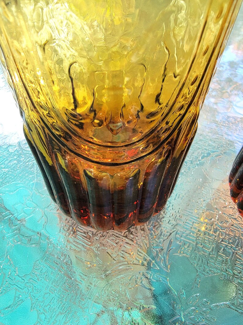 May include: A pair of amber glass tumblers with a textured, ribbed design. The glasses have a rounded bottom and a wide mouth.