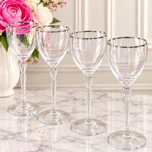 May include: A set of four clear glass wine glasses featuring a thin silver rim at the top and a textured, diamond-patterned stem. Each glass has a smooth, rounded bowl and a circular base, showcasing a refined and elegant design for serving beverages.