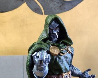 Puede incluir: Una figura detallada y pintada a mano del Doctor Doom, un supervillano de Marvel Comics. Lleva una capa verde y una máscara de metal, y está de pie sobre una base rocosa.