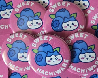 May include: A collection of pink round buttons with a blueberry and character design. The buttons have the word "SWEET" in white and the text "HACHIWARE" in black. The blueberries are blue with green leaves.