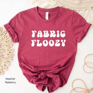 Pu&ograve; includere: T-shirt color lampone con la scritta bianca "FABRIC FLOOZY" in un font retr&ograve;. Le maniche sono arrotolate e la maglietta &egrave; annodata in vita. La parola "Canvas" &egrave; stampata sull'etichetta.