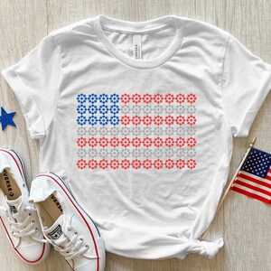 May include: White t-shirt with a red, white, and blue American flag design made of small stars. The flag is centered on the shirt.