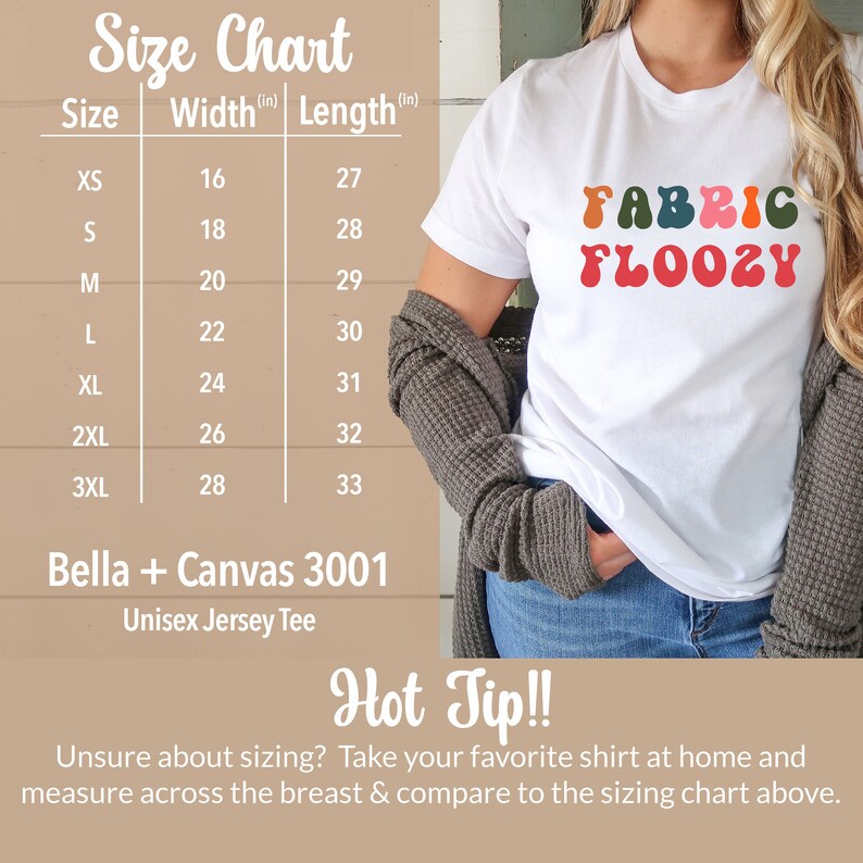 Pu&ograve; includere: T-shirt unisex bianco con la scritta "FABRIC FLOOZY" in un font retr&ograve; colorato. Una tabella delle taglie mostra le misure di larghezza e lunghezza in centimetri. La maglietta &egrave; Bella + Canvas 3001.