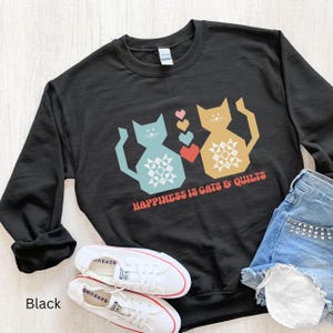 May include: Black sweatshirt with a graphic of two cats holding a heart. The text "Happiness is cats & quilts" is printed on the sweatshirt.