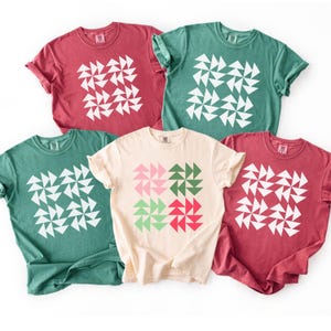 May include: Five t-shirts in various colors: red, green, and cream. Each shirt features a white geometric design. The design is made up of triangles arranged in a square pattern. The shirts are casual and comfortable.