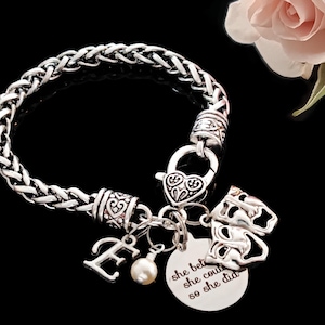 May include: A silver-toned wheat chain bracelet featuring a heart-shaped lobster clasp, a letter E charm, a small white pearl bead, a comedy and tragedy mask charm, and a round metal disc engraved with the text she believed she could so she did.