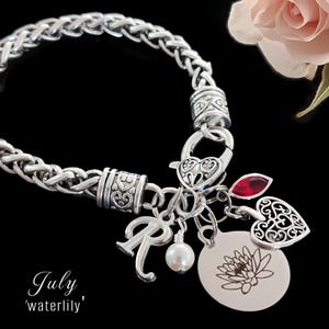 May include: A silver-toned bracelet with a braided chain design. Charms include a letter "R", a pearl, a heart, a red gem, and a round charm with a lotus flower. The text "July 'waterlily'" is at the bottom left.