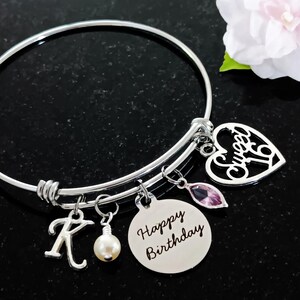 May include: Silver charm bracelet with a heart charm that says "Sweet 16", a round charm that says "Happy Birthday", a letter K charm, and a pearl charm.