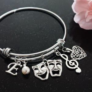 May include: A silver charm bracelet with a variety of charms, including a heart, a musical note, two theater masks, a pearl, and a letter E.