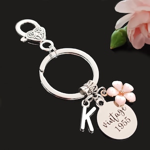 May include: Silver keychain with a charm that says "vintage 1955" and a pink flower charm. The keychain also has a letter K charm.