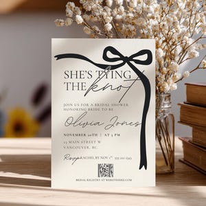 Könnte beinhalten: Cremefarbene Brautparty-Einladung mit dem Text "She's Tying the Knot" und dem Namen "Olivia Jones". Die Einladung zeigt ein schwarzes Schleifendesign und enthält Datum, Uhrzeit und Ort der Veranstaltung.