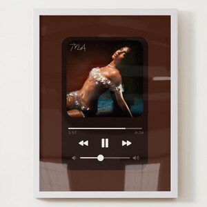 May include: Framed art print featuring a stylized image of a person in a music player interface. The image has the name "TYLA" at the top. The player controls and progress bar are visible at the bottom. The artwork is set against a brown background.