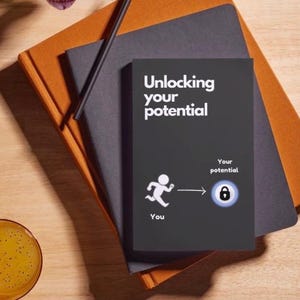 May include: A black notebook with the text "Unlocking your potential" and an illustration of a person running towards a lock. The notebook is on top of a gray and orange notebook.