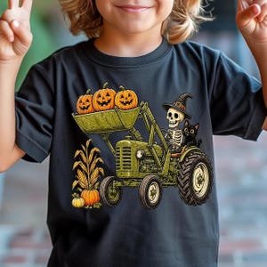 May include: A black t-shirt featuring a graphic of a skeleton wearing a witch hat and a black cat driving a green tractor. The tractor bucket holds three orange jack-o'-lanterns, and a corn stalk with a pumpkin sits beside the tractor wheels.
