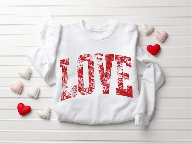 A white long-sleeved shirt with the word "LOVE" printed in red text, along with a few small heart-shaped objects surrounding it.