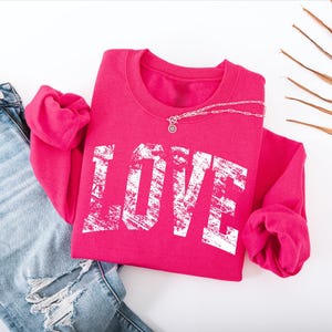 A pink sweatshirt with the word "LOVE" printed on it, along with a pair of blue jeans and some dried leaves or branches.