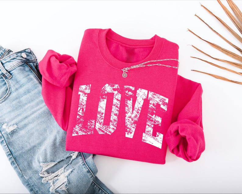 A pink sweatshirt with the word "LOVE" printed on it, along with a pair of blue jeans and some dried leaves or branches.