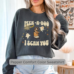May include: A gray sweatshirt with a vintage-style graphic of a ghost peeking out from behind an ultrasound machine. The text reads "Peek-a-Boo I Scan You".