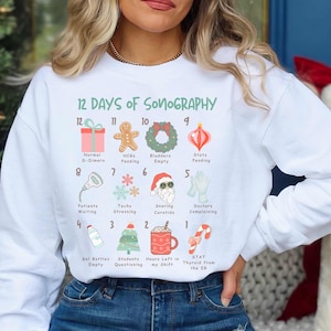 May include: White sweatshirt with a festive design featuring the 12 Days of Sonography. The design includes a countdown from 12 to 1 with various sonography-related items, such as a fetal heartbeat monitor, a Christmas tree, and a Santa Claus with a stethoscope.