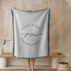 May include: A light grey throw blanket with a fringed edge. The blanket features a circular design with the names "JESSICA & CHRIS", the initials "J♡C", and the date "20TH SEPTEMBER 2025" in black script.