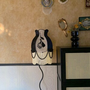 May include: A black and white lampshade with a black rose design and white fringe. The lampshade is on a black metal stand.