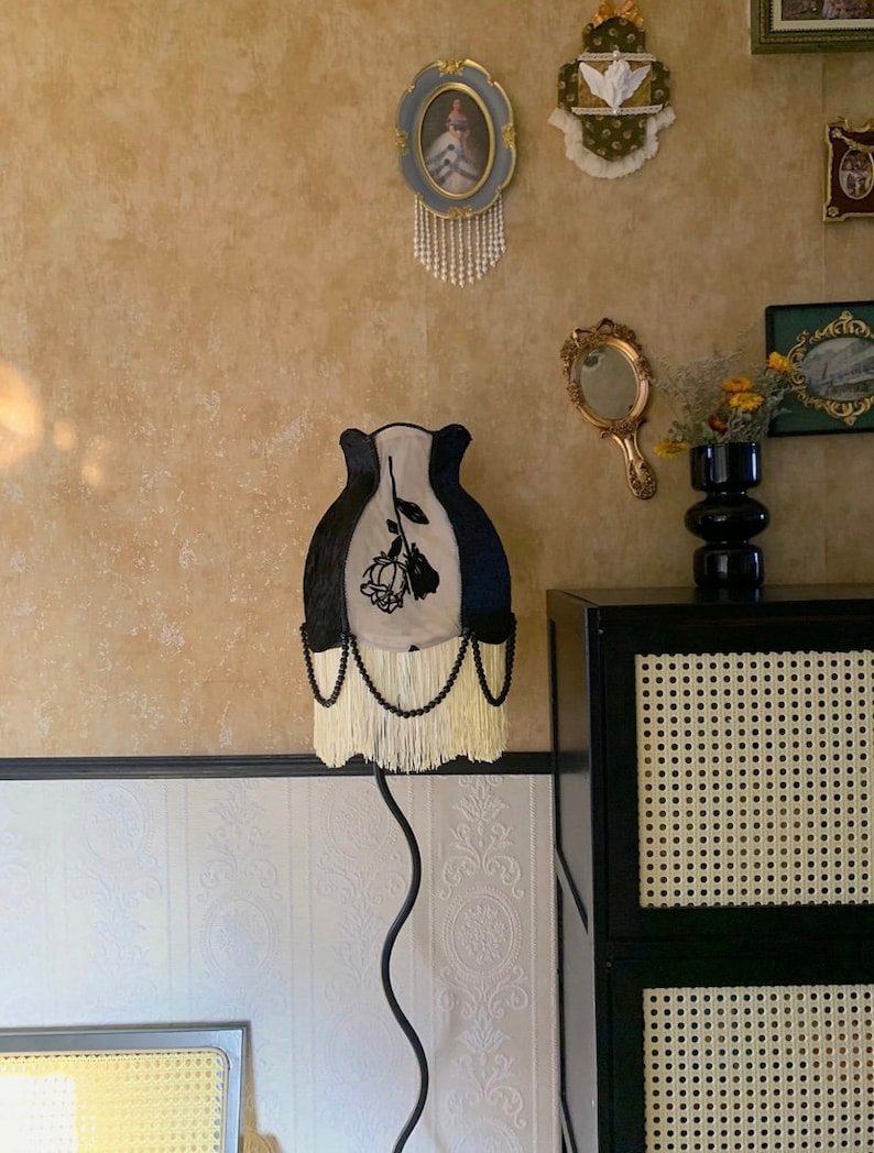 May include: A black and white lampshade with a black rose design and white fringe. The lampshade is on a black metal stand.