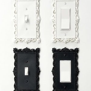 Pode incluir: Quatro capas decorativas para interruptores de luz. Duas são brancas com molduras ornamentadas e duas são pretas com molduras semelhantes. Cada capa tem um interruptor branco. As molduras têm um design floral detalhado.