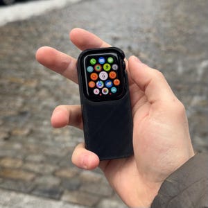 May include: A black protective case for an Apple Watch with a textured surface. The watch face is visible and shows a variety of app icons.
