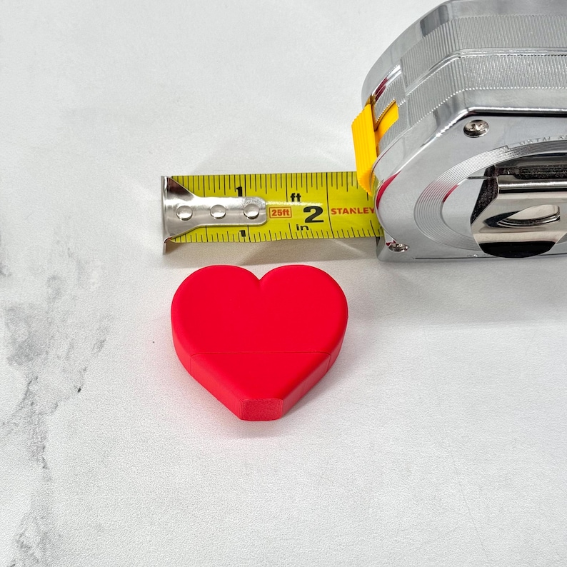 May include: A red heart-shaped object is measured with a yellow tape measure that reads "25ft" and "2 in". The tape measure is a Stanley brand.