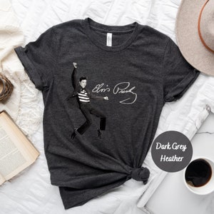 Op de afbeelding: Donkergrijs heather t-shirt met een zwart-witte afbeelding van Elvis Presley met zijn handtekening. De afbeelding toont Elvis in een zwart-wit gestreept shirt, een zwarte broek en zwarte schoenen, met zijn armen in de lucht.