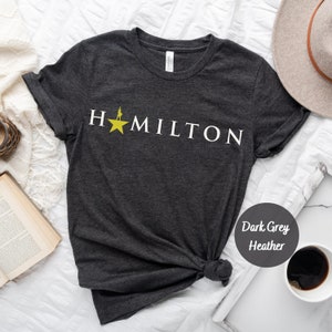 Op de afbeelding: Donkergrijs heather t-shirt met een witte afbeelding van een ster en het woord "HAMILTON".