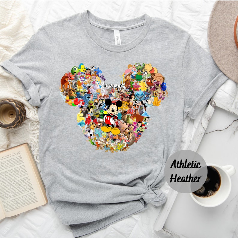 May include: A gray t-shirt with a Mickey Mouse silhouette made up of various Disney characters. The text "Athletic Heather" is printed on the bottom right corner of the shirt.
