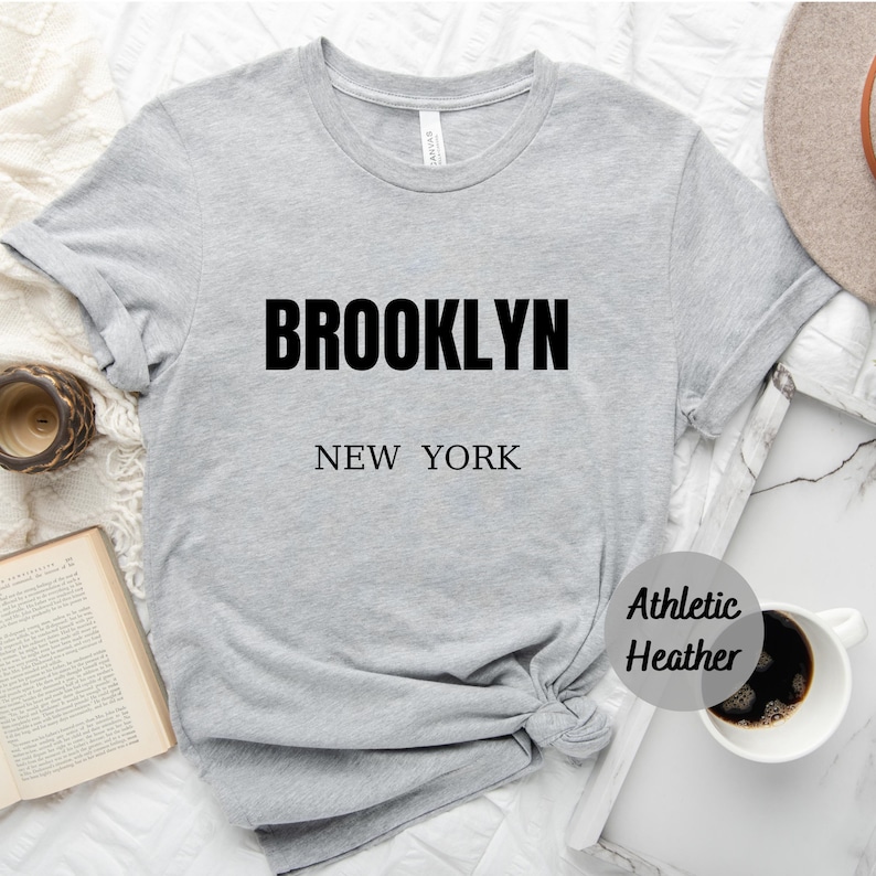 May include: Gray t-shirt with black text that reads "BROOKLYN NEW YORK" in a simple, modern font. The shirt is made of a soft, comfortable material and has a relaxed fit.