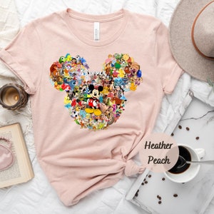 May include: A pink t-shirt with a graphic of Mickey Mouse's ears made up of various Disney characters. The text "Heather Peach" is printed on the bottom right corner of the shirt.