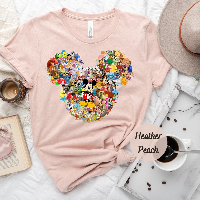 May include: A pink t-shirt with a graphic of Mickey Mouse's ears made up of various Disney characters. The text "Heather Peach" is printed on the bottom right corner of the shirt.