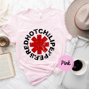 May include: Pink t-shirt with a black and red Red Hot Chili Peppers logo. The logo is a red star with a black outline and the words "Red Hot Chili Peppers" around it.
