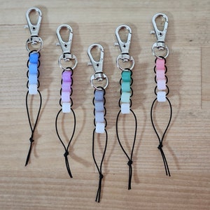 May include: Five colorful beaded keychains with silver key rings and black cords. The beads are ombre, with each keychain featuring a different color gradient.