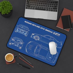 Peut inclure: Tapis de souris bleu avec un plan de conception d'une Nissan Skyline GT-R (BNR34) Z-Tune. Le design présente des dessins au trait blancs de la voiture sur un fond quadrillé bleu. Une souris d'ordinateur blanche est posée sur le tapis.