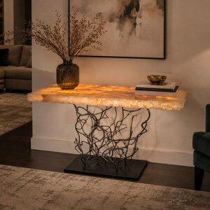 May include: A rectangular console table featuring a thick, translucent, amber-toned stone top that emits a warm internal glow. The base is constructed from a complex, dark metal structure resembling tangled branches, supported by a flat, rectangular base.