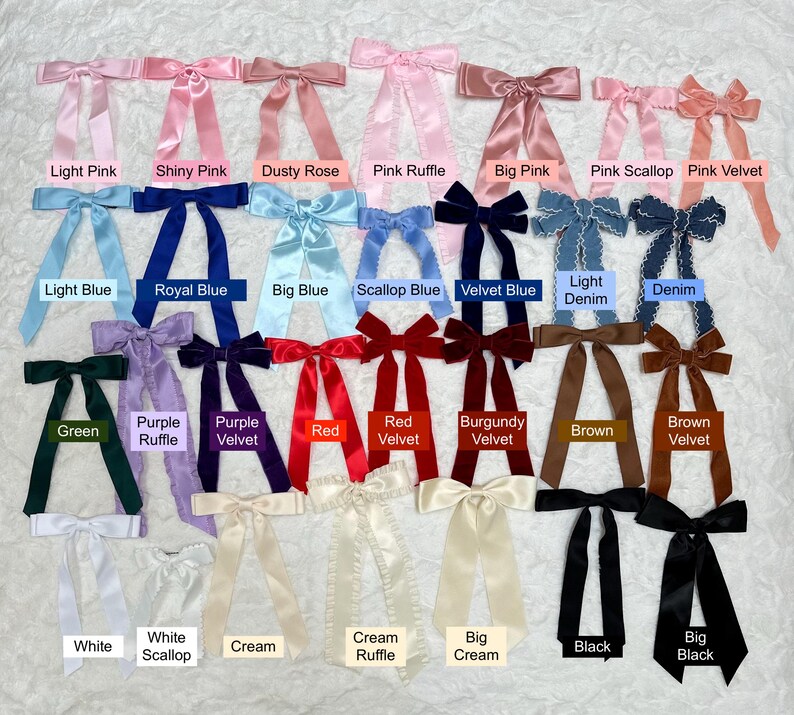 Peut inclure: Un assortiment de n&oelig;uds en tissu pour cheveux dans diff&eacute;rentes couleurs et styles, y compris des couleurs unies, du velours, des volants et des coquillages. Les n&oelig;uds sont dispos&eacute;s en rang&eacute;es sur une surface blanche.