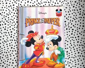 May include: A vintage Disney's "The Prince and the Pauper" book. The cover features Mickey Mouse in royal attire, with the title in gold lettering. The background is a pink and white striped design. The book is on a black and white polka dot background.
