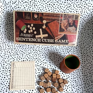 May include: A vintage Scrabble Sentence Cube Game in its original box. The box features a photo of a couple playing the game. The game includes wooden cubes with words printed on each side, a score sheet, and a cup.