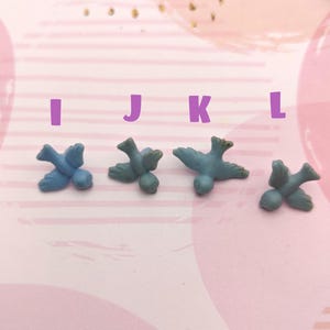 May include: Four blue bird figurines, each with a slightly different pose, are arranged in a row on a pink and white striped surface. The figurines are small and delicate, with a matte finish.