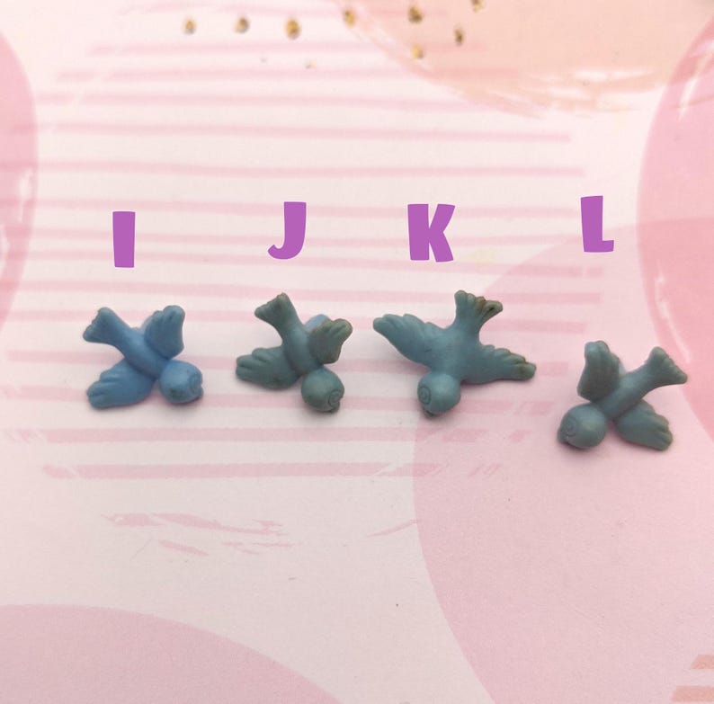 May include: Four blue bird figurines, each with a slightly different pose, are arranged in a row on a pink and white striped surface. The figurines are small and delicate, with a matte finish.