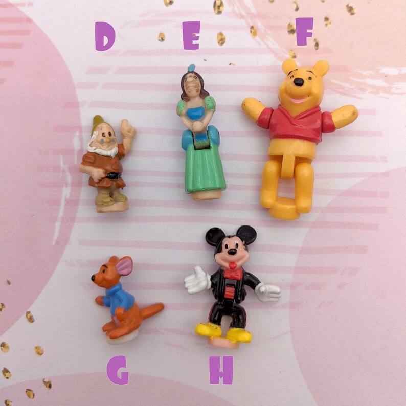 May include: A set of eight small plastic figurines of Disney characters. The characters include Snow White, a dwarf, Winnie the Pooh, Mickey Mouse, and a kangaroo. The figurines are all in different poses and are painted in bright colors.