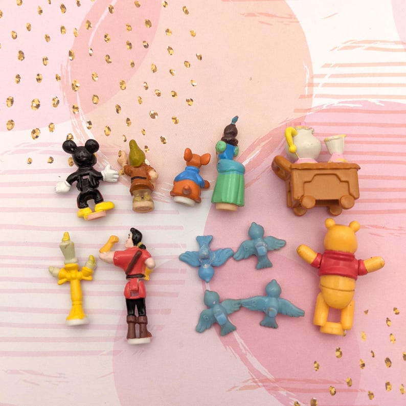 May include: A collection of 10 small plastic figurines, including Mickey Mouse, a dwarf, a princess, a teapot, a bird, and Winnie the Pooh. The figurines are all in different poses and are painted in bright colors.