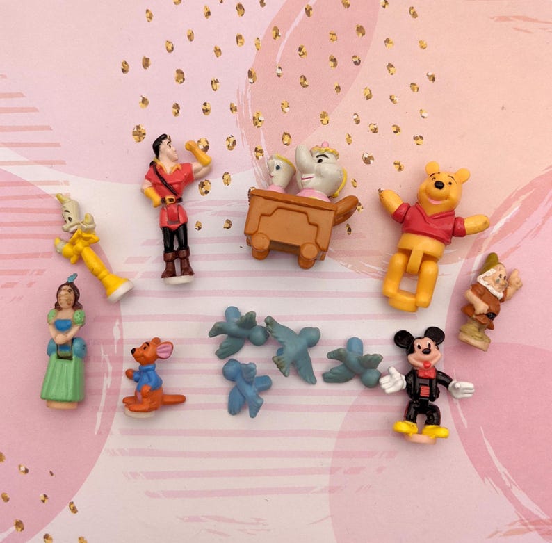 May include: A collection of small plastic Disney character figurines, including Winnie the Pooh, Mickey Mouse, Belle, and the Beast. There are also several blue bird figurines and a small brown figurine of a kangaroo.