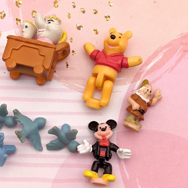 May include: A set of small plastic Disney character figurines, including Mickey Mouse, Winnie the Pooh, and a dwarf. The figurines are yellow, red, black, brown, and blue.