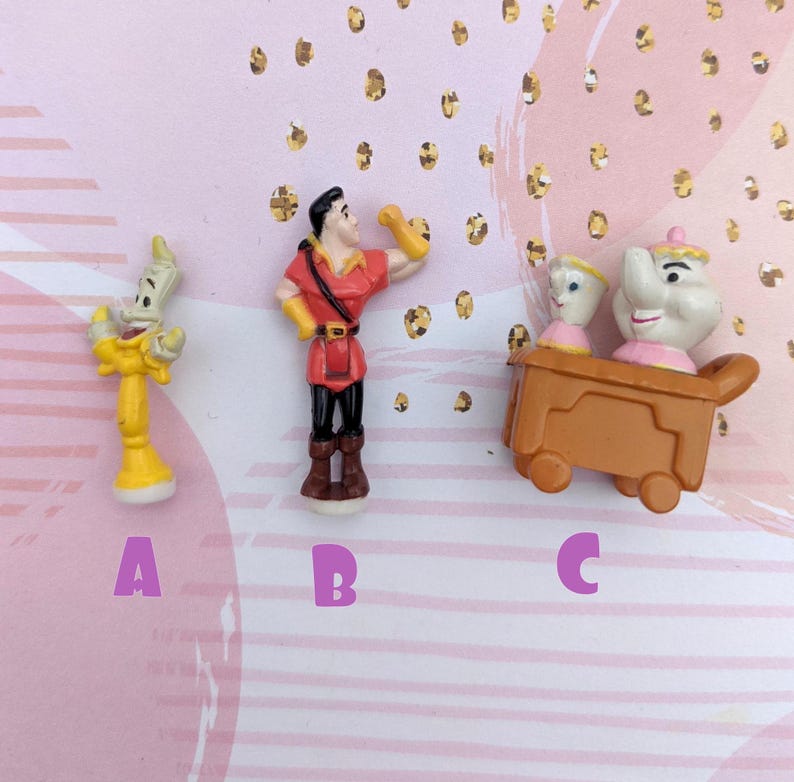 May include: Three small plastic figurines from the Disney movie Beauty and the Beast. The figurines are of Belle, the Beast, and Lumiere. The figurines are yellow, red, and white.
