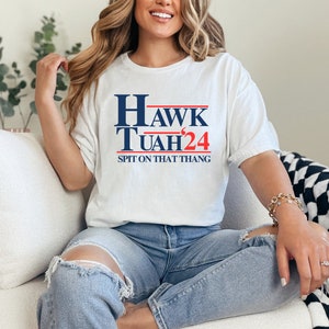 May include: White t-shirt with blue and red text that reads "HAWK TUAH'24" and "SPIT ON THAT THANG".